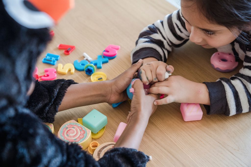 Two children in animal costumes play with colorful toys on a wooden table.